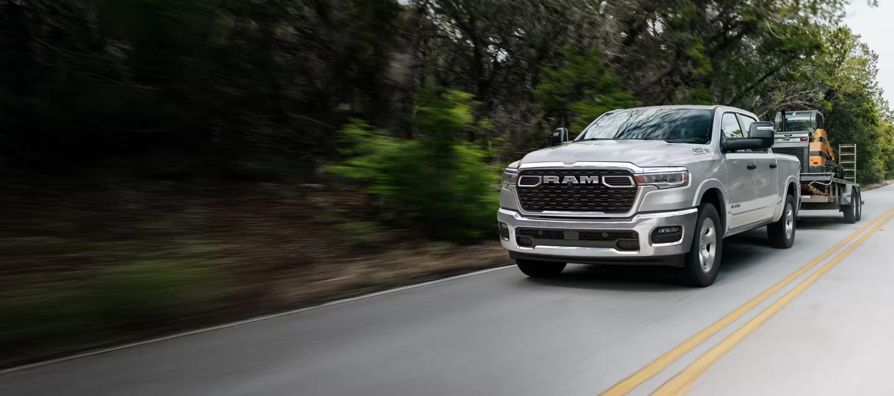 A silver pickup truck towing a trailer driving on a tree-lined road.