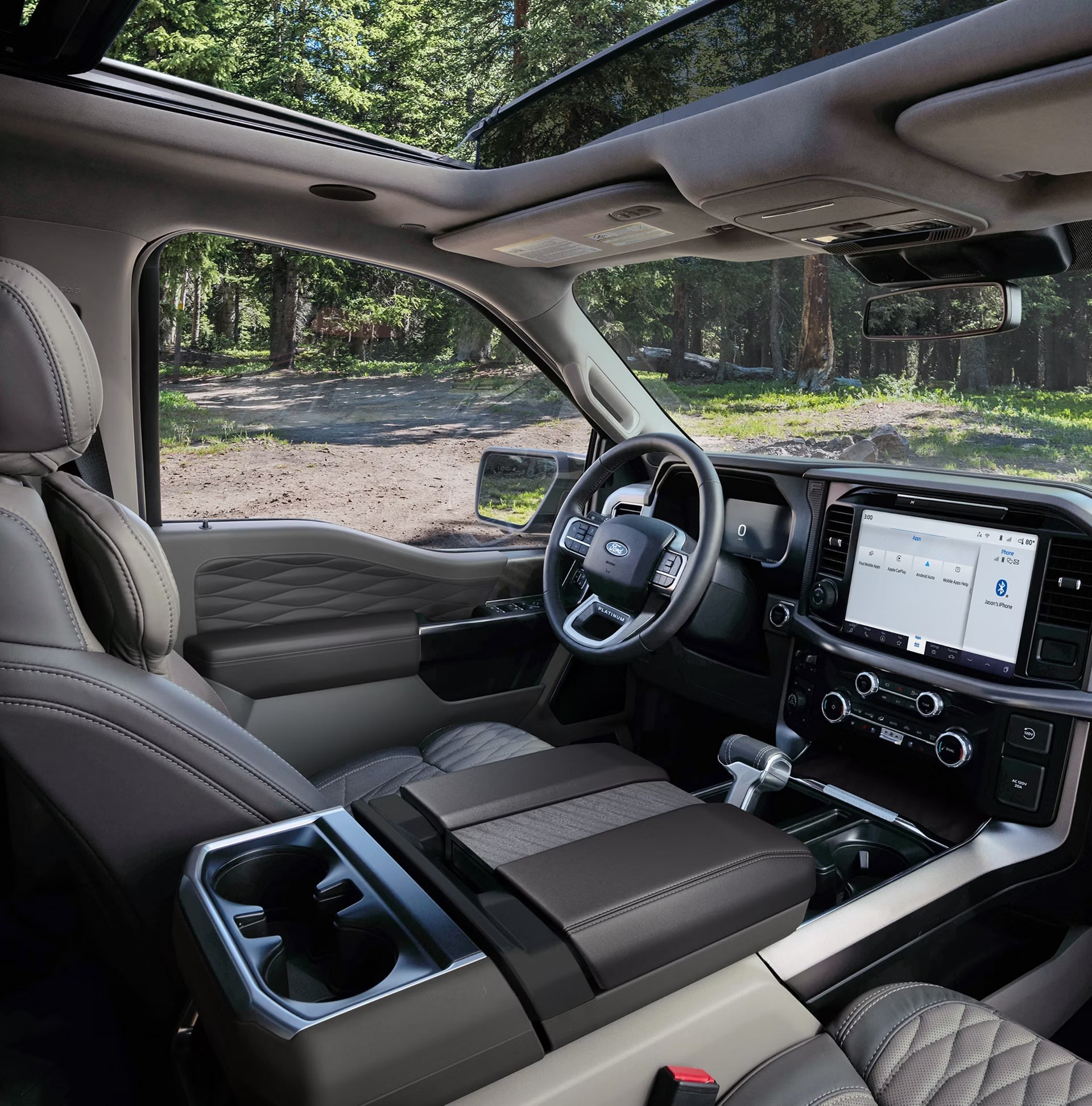 Luxurious interior of a modern truck with quilted leather seats and a large touchscreen, with a backdrop of a sun-dappled forest road.