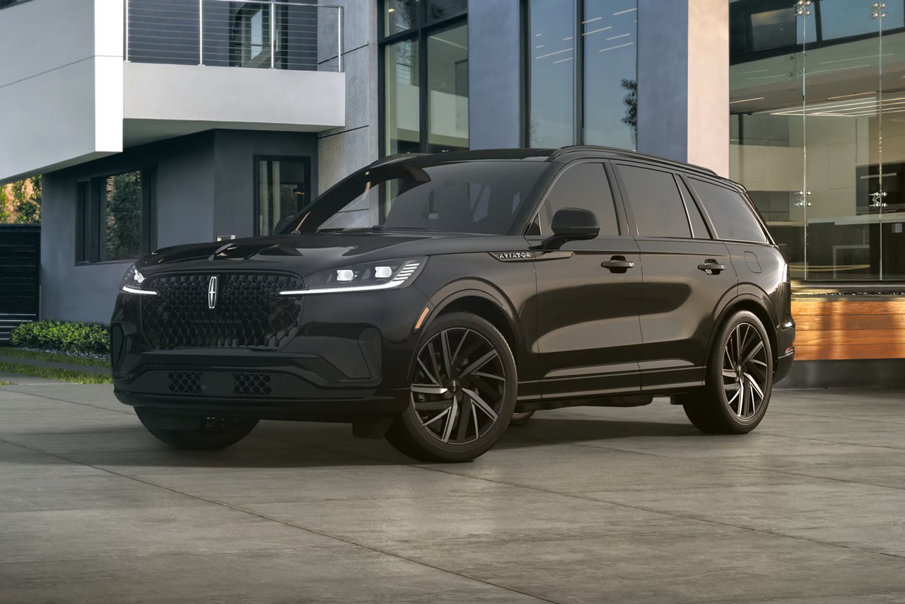 A large black SUV parked in front of a modern glass-fronted building.