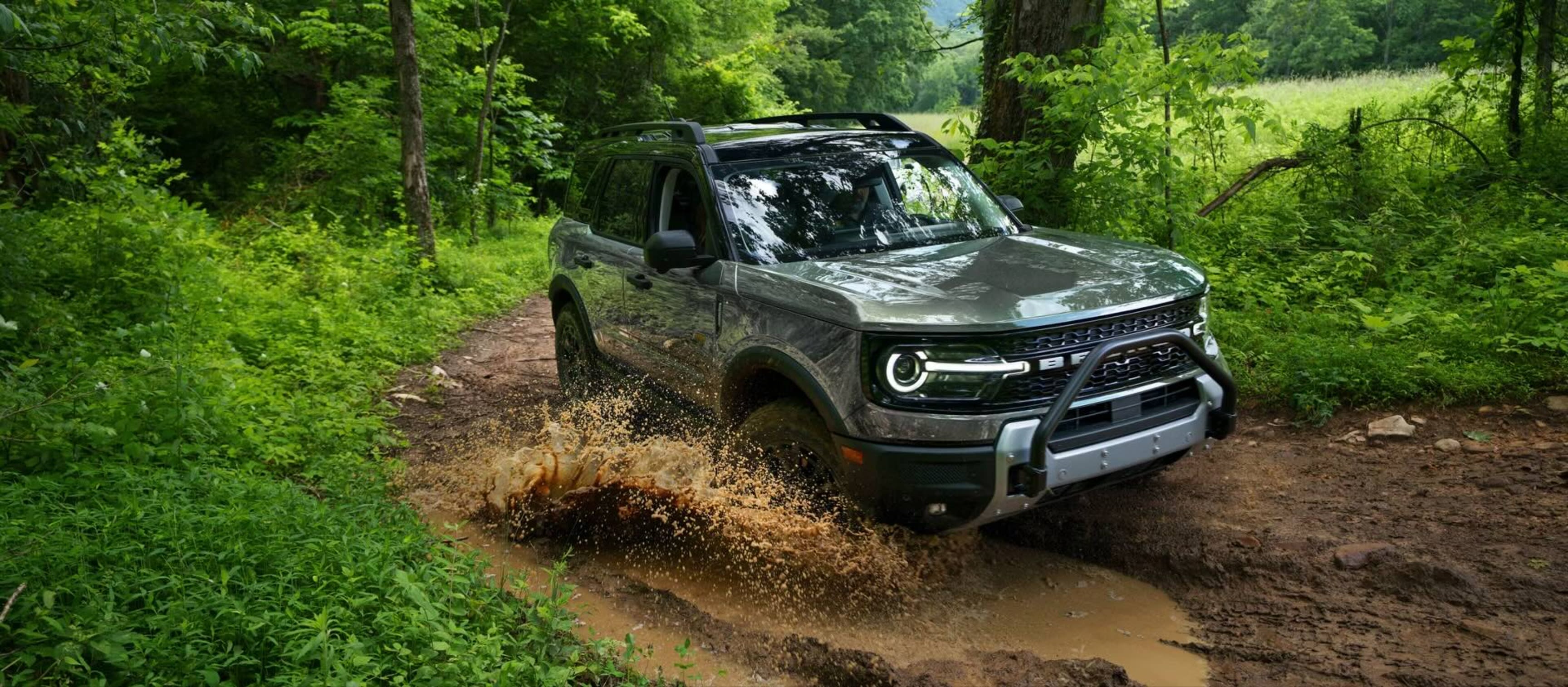 An SUV driving through a muddy trail in a lush green forest.