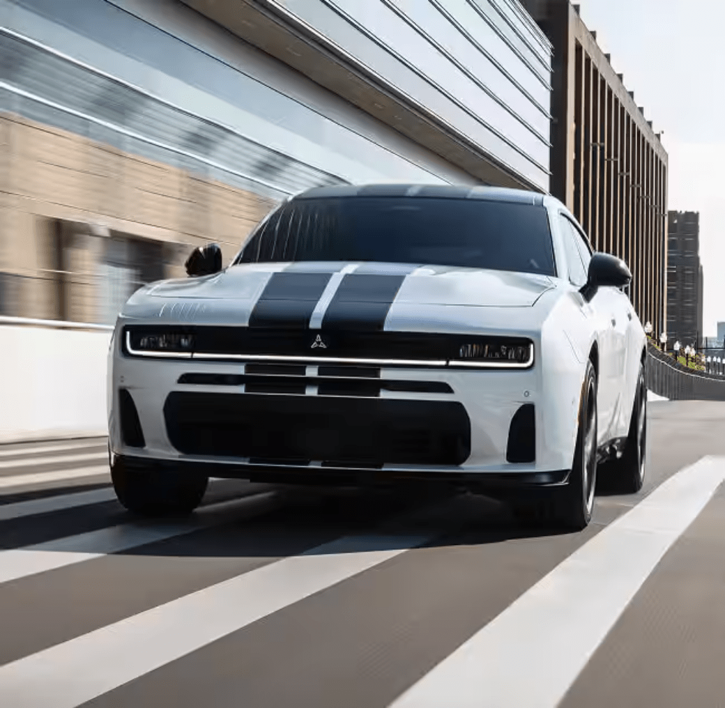 A white sports car with black racing stripes driving past modern architectural buildings.