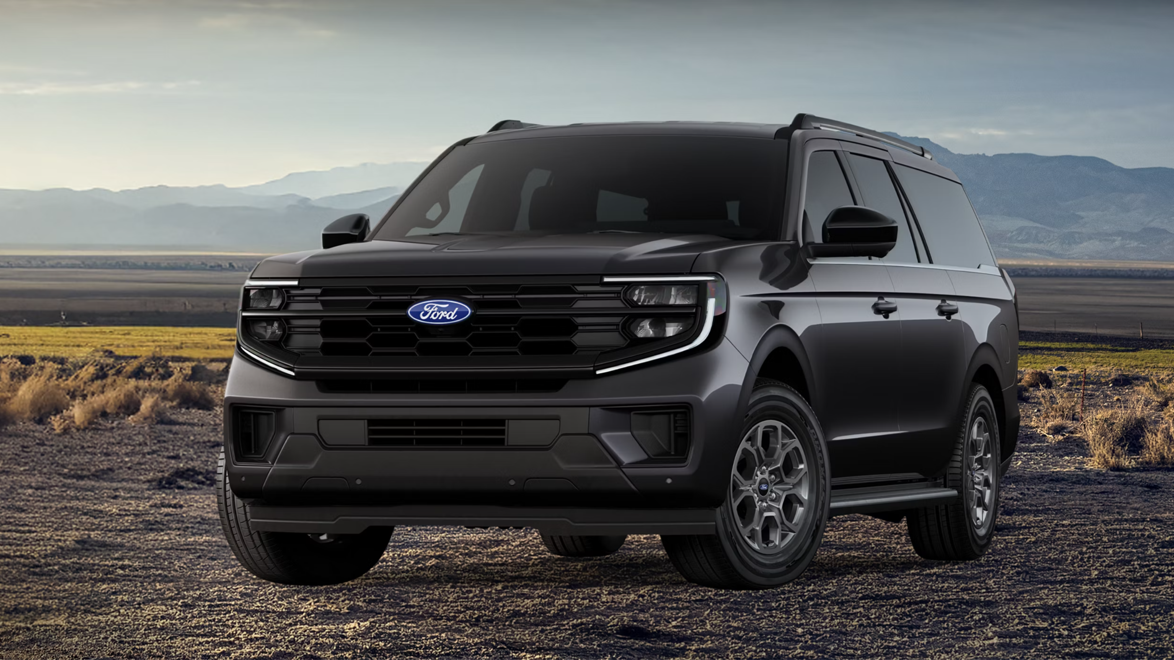 A dark grey SUV parked in the desert with mountains in the background.