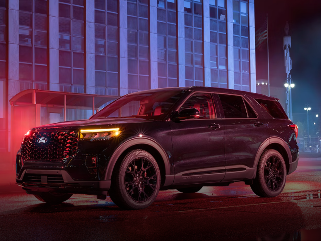 A sleek black SUV parked on a city street at night in front of a tall, modern building with glowing windows.