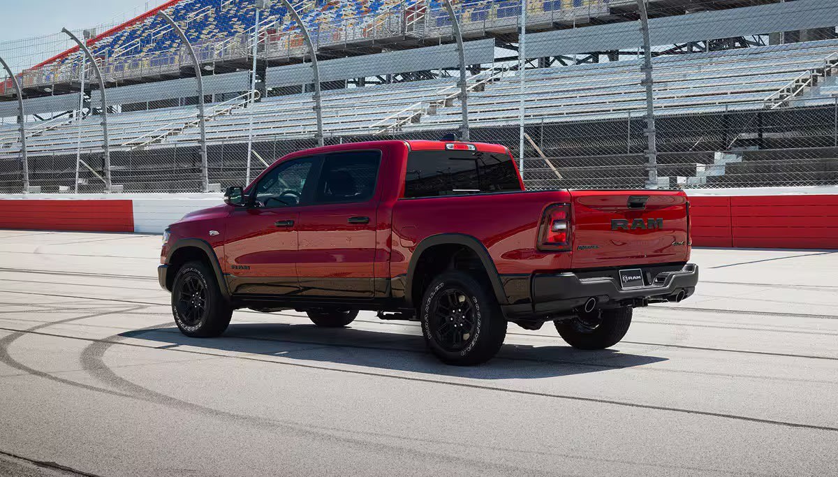 A red pickup truck is parked on a paved track in front of empty stadium bleachers.