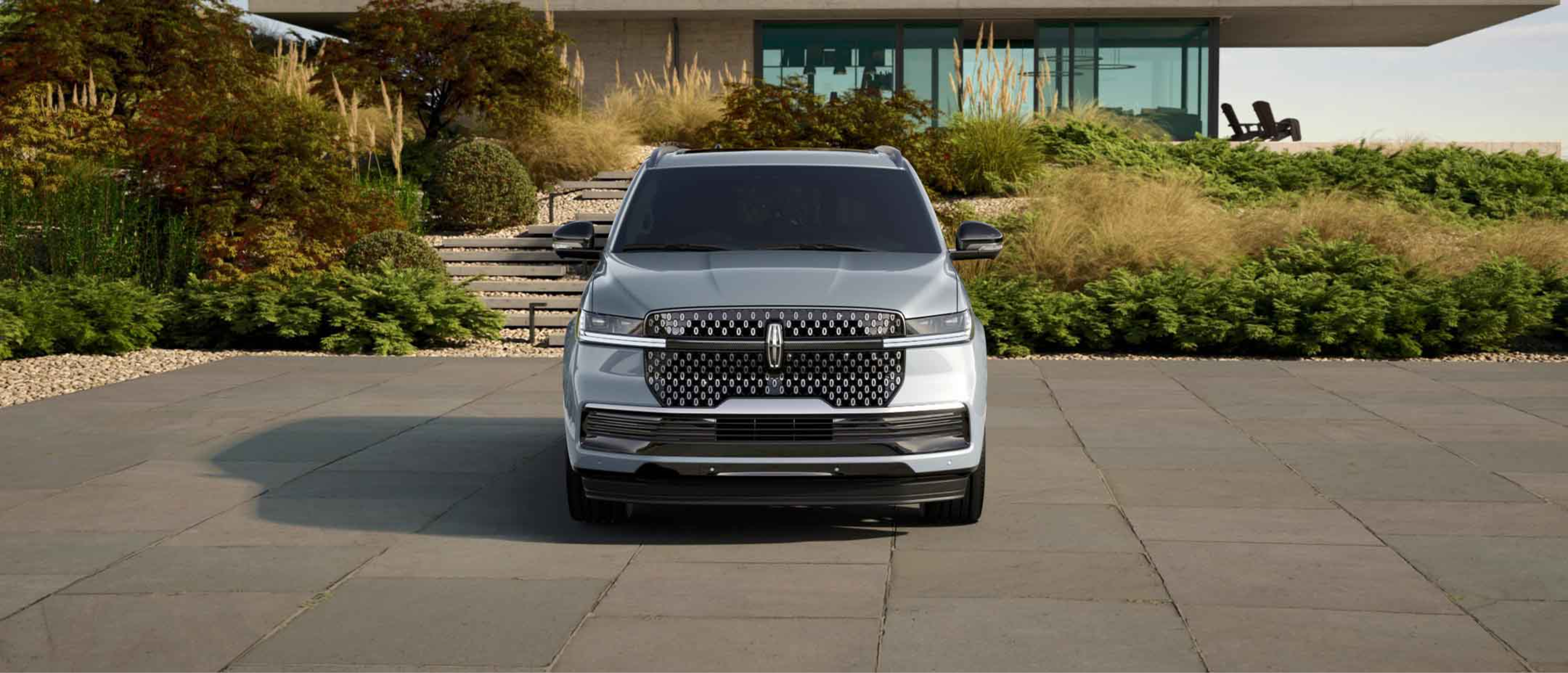 A silver SUV parked on a paved driveway in front of a modern house with lush landscaping.