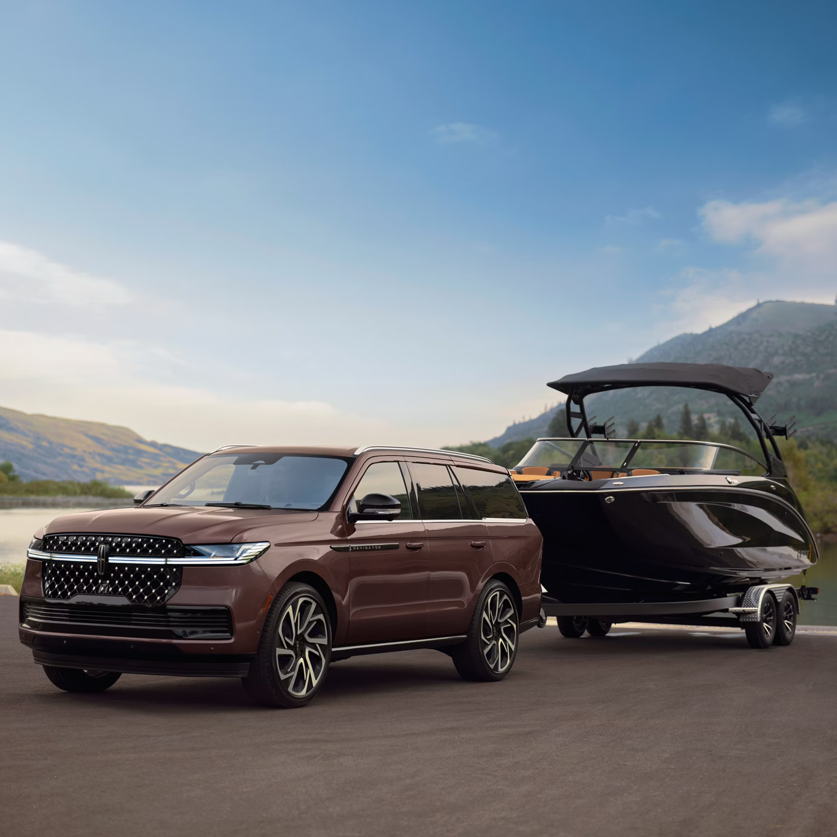 A brown SUV tows a boat on a trailer, with a serene lake and rolling hills under a blue sky in the background.