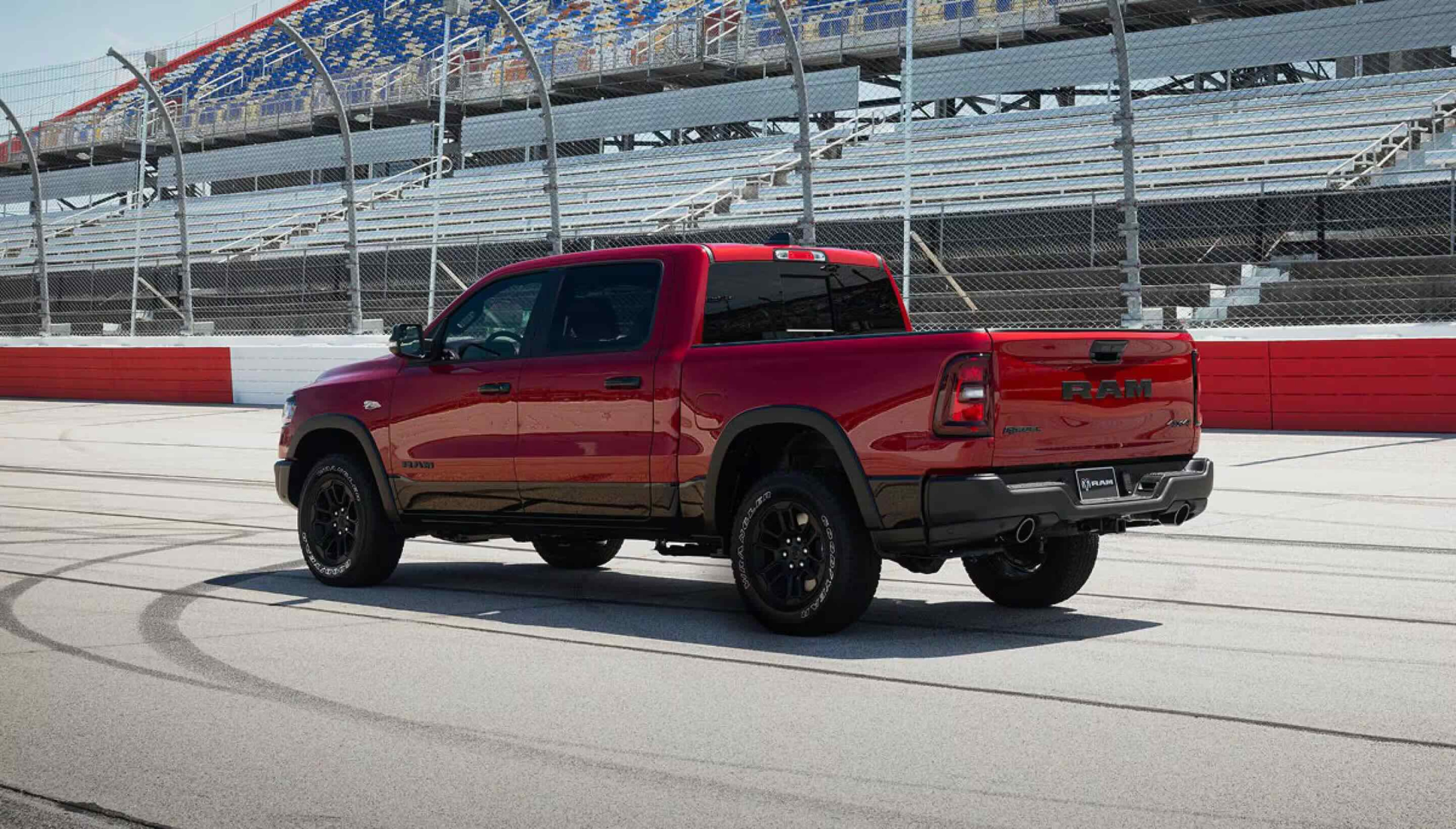A red pickup truck is parked on a racetrack with tire marks on the asphalt, while grandstands are visible in the background.