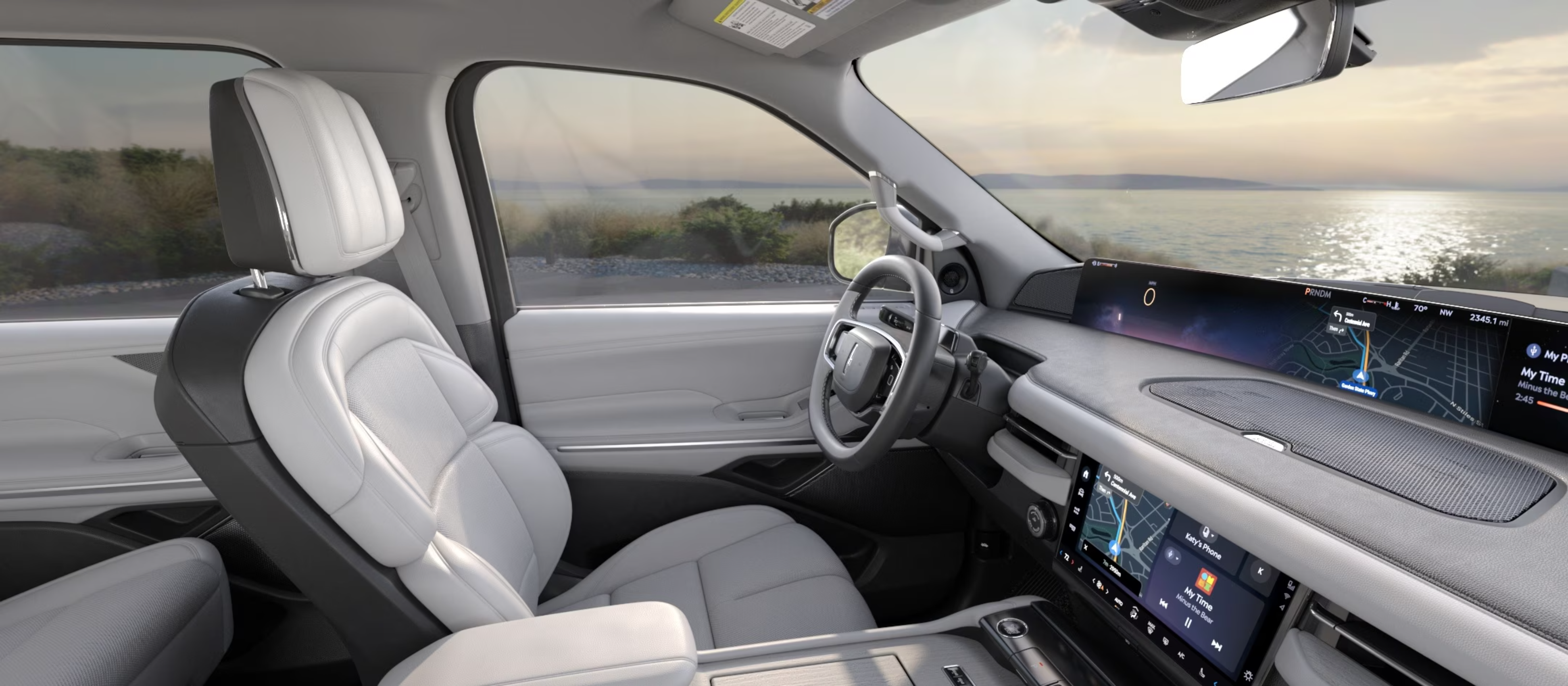 Luxurious car interior with white leather seats against a serene ocean view at sunset.