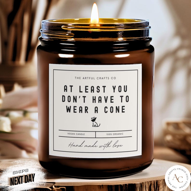 Lit amber recovery candle that says At Least You Don't Have to Wear a Cone