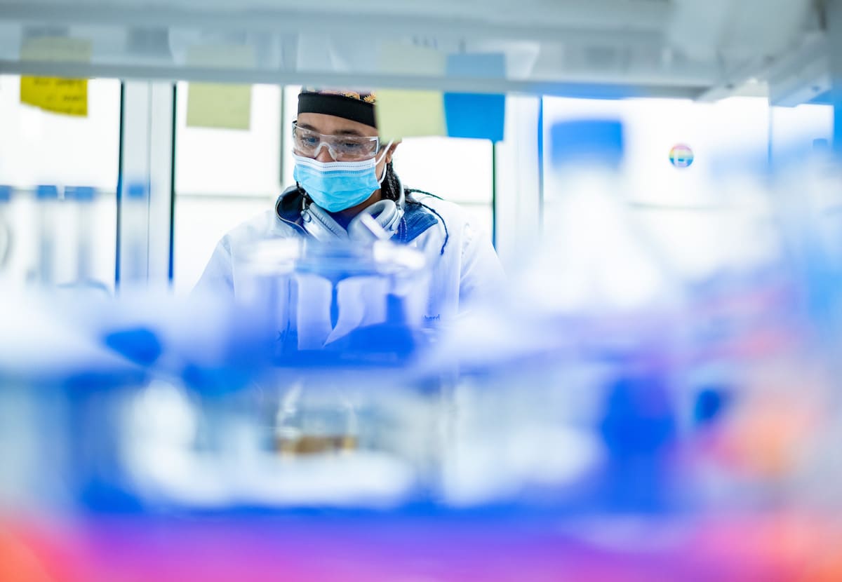 A person working in a lab with a surgical mask and safety google