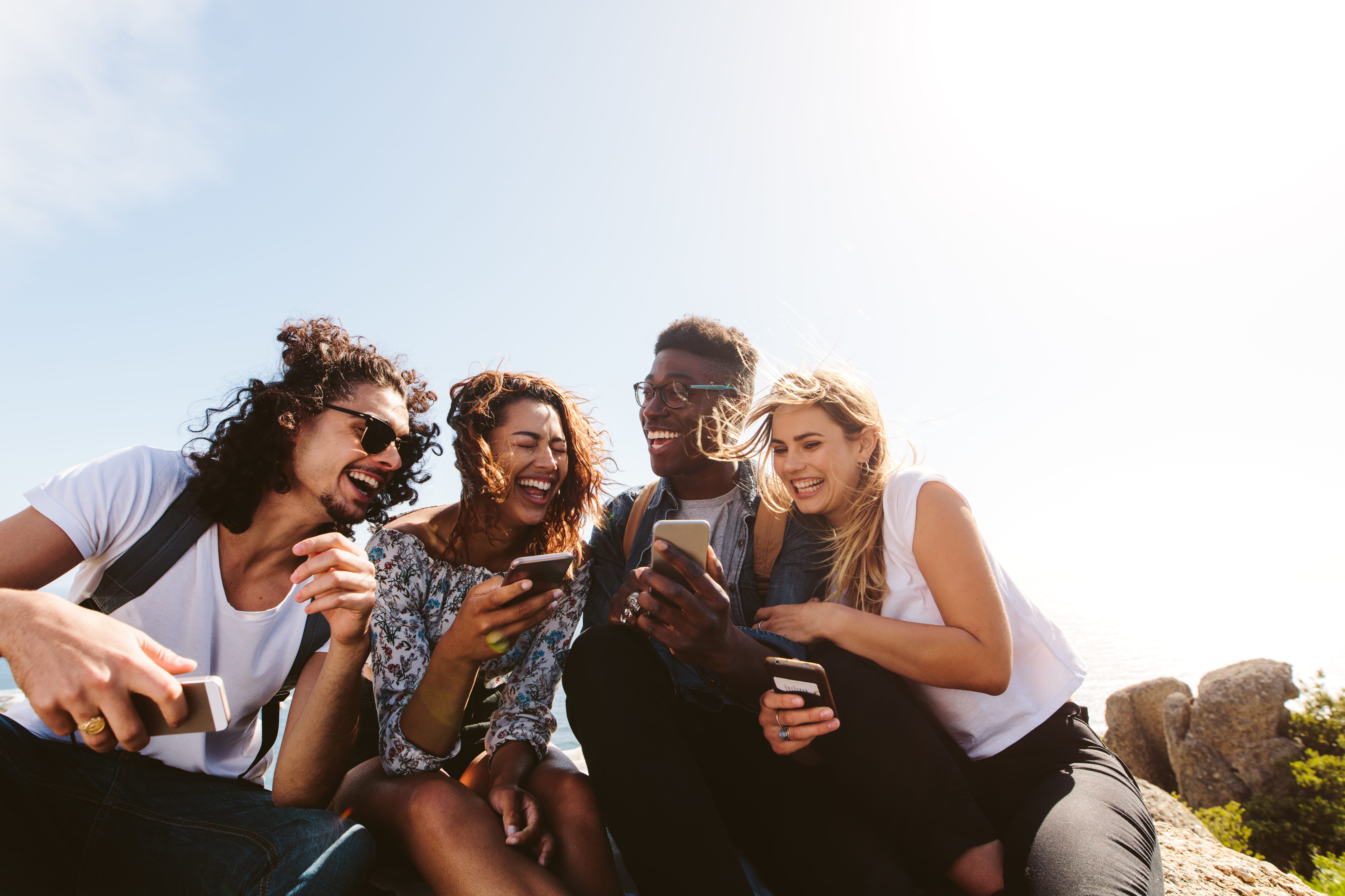 Group of young friends laughing together while using their phones