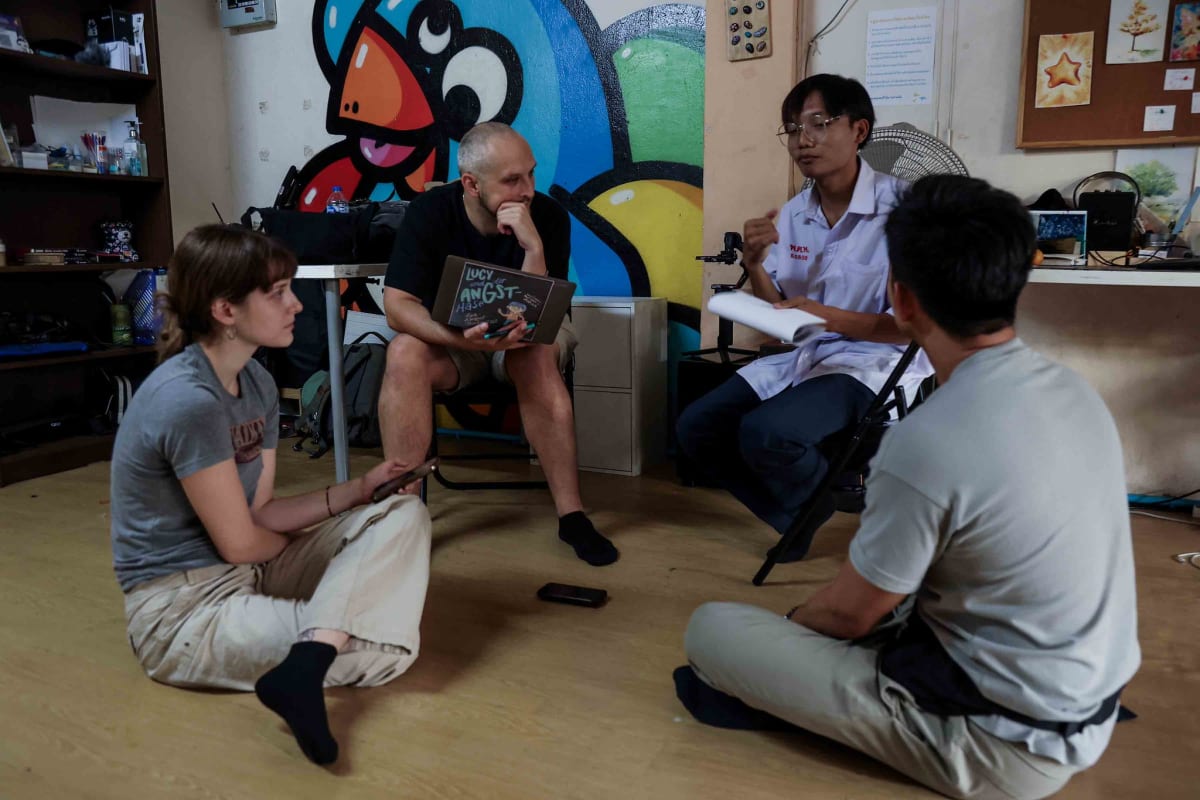 Two documentary filmmakers and two local changemaker staff sit in conversation during pre-production research in Thailand, surrounded by colorful murals.