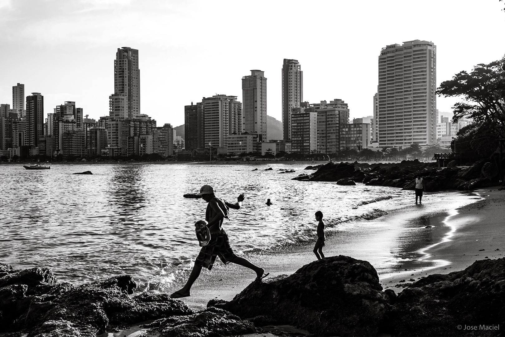 Man walks from one rock to the other on a beach. Black and white
