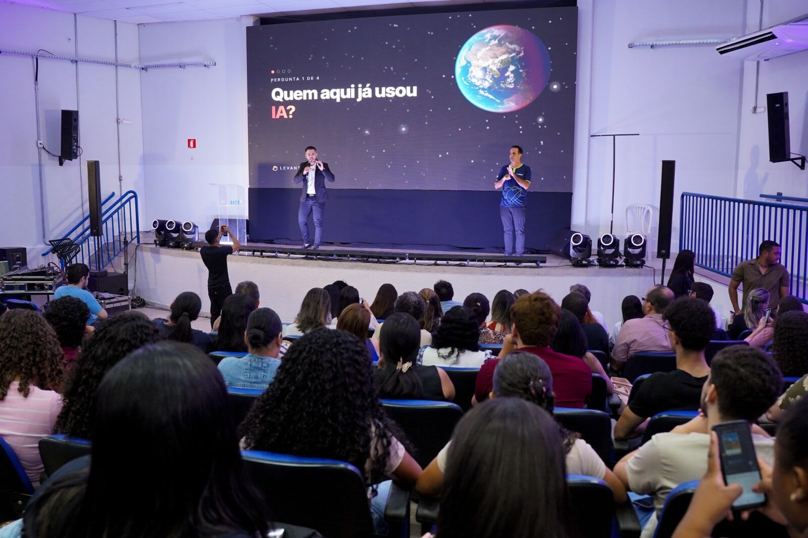 Auditório da UnirG lotado durante a palestra de Luiz Carvalho, com o slide Quem aqui já usou IA e o globo terrestre no telão