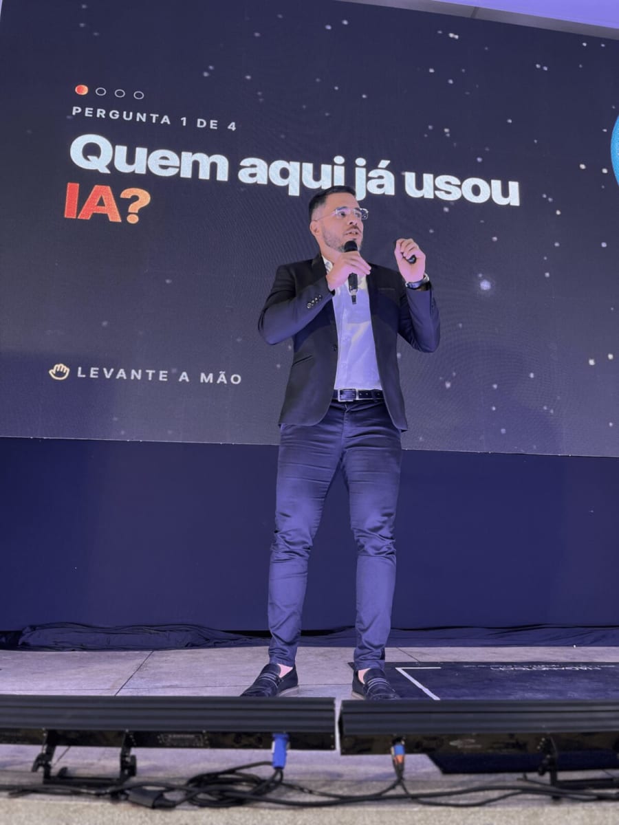 Luiz Carvalho no palco com o slide Pergunta 1 de 4: Quem aqui já usou IA? Levante a mão