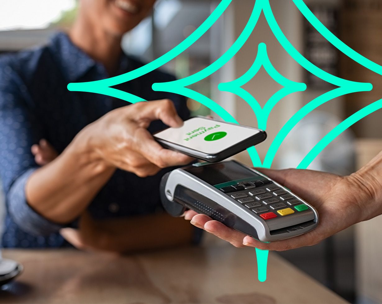 Smiling customer taps a smartphone showing "Payment Sent" on a handheld card terminal to complete a contactless payment at a shop counter