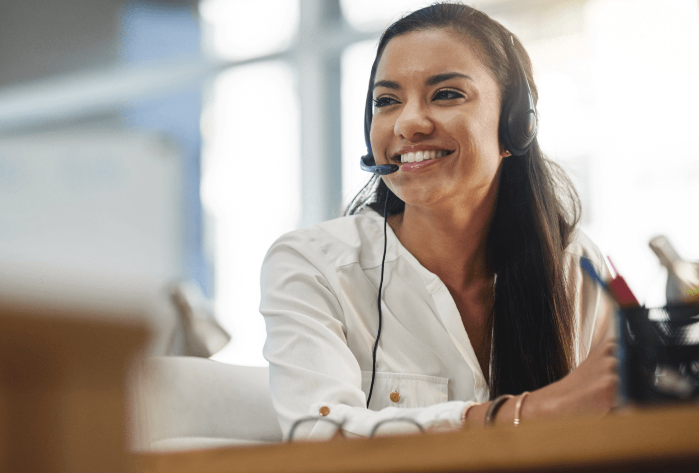 Smiling contact center agent wearing a headset at her desk in a bright office