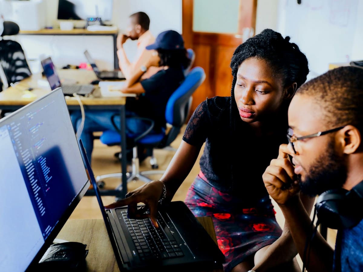 Three students working together on a laptop, one pointing at the screen