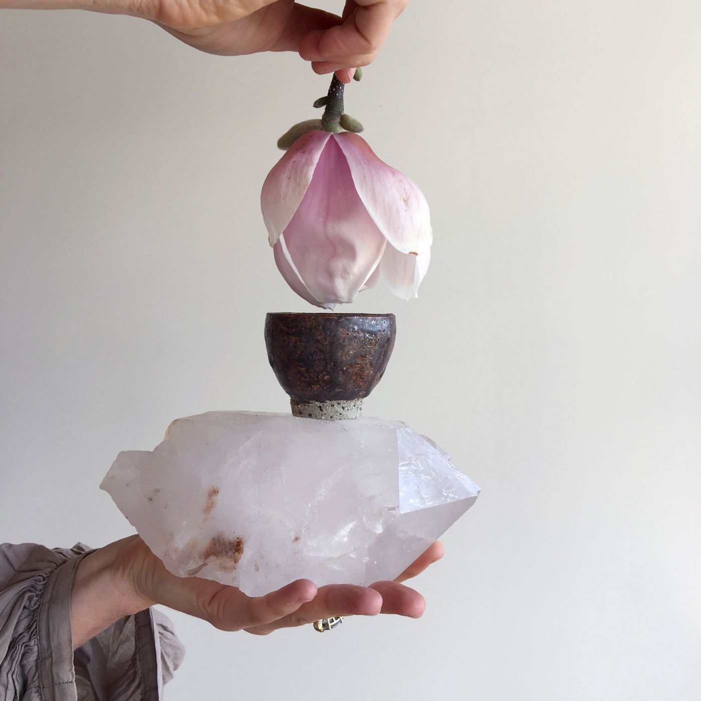 A hand dipping a flower into a small cacao bowl on top of a large crystal held by the other hand