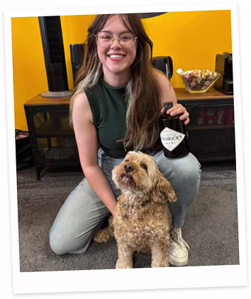 Tabs kneeling in an office setting, smiling while holding Sherlock, a fluffy dog.