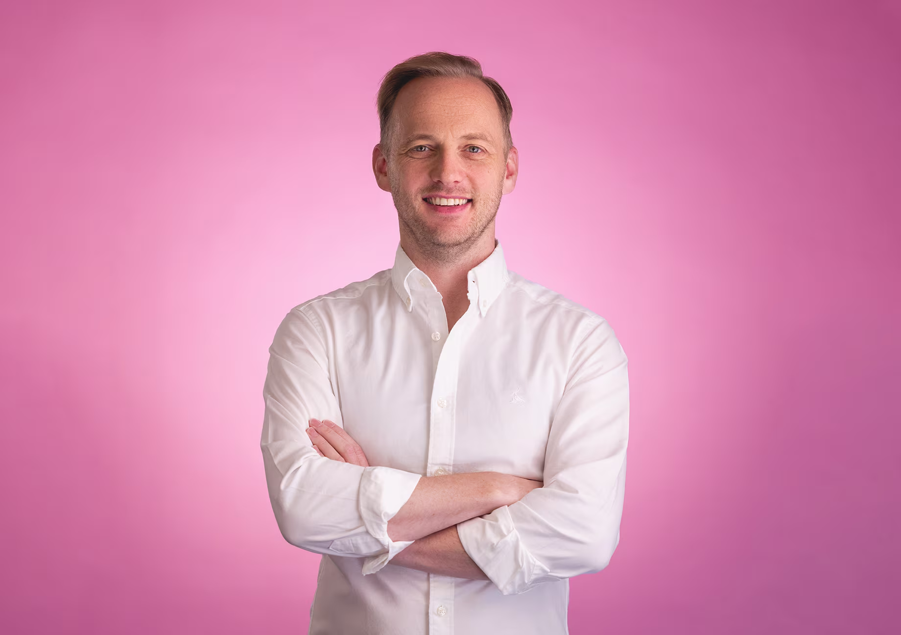 Chris Nicholl standing with arms crossed in front of pink backdrop