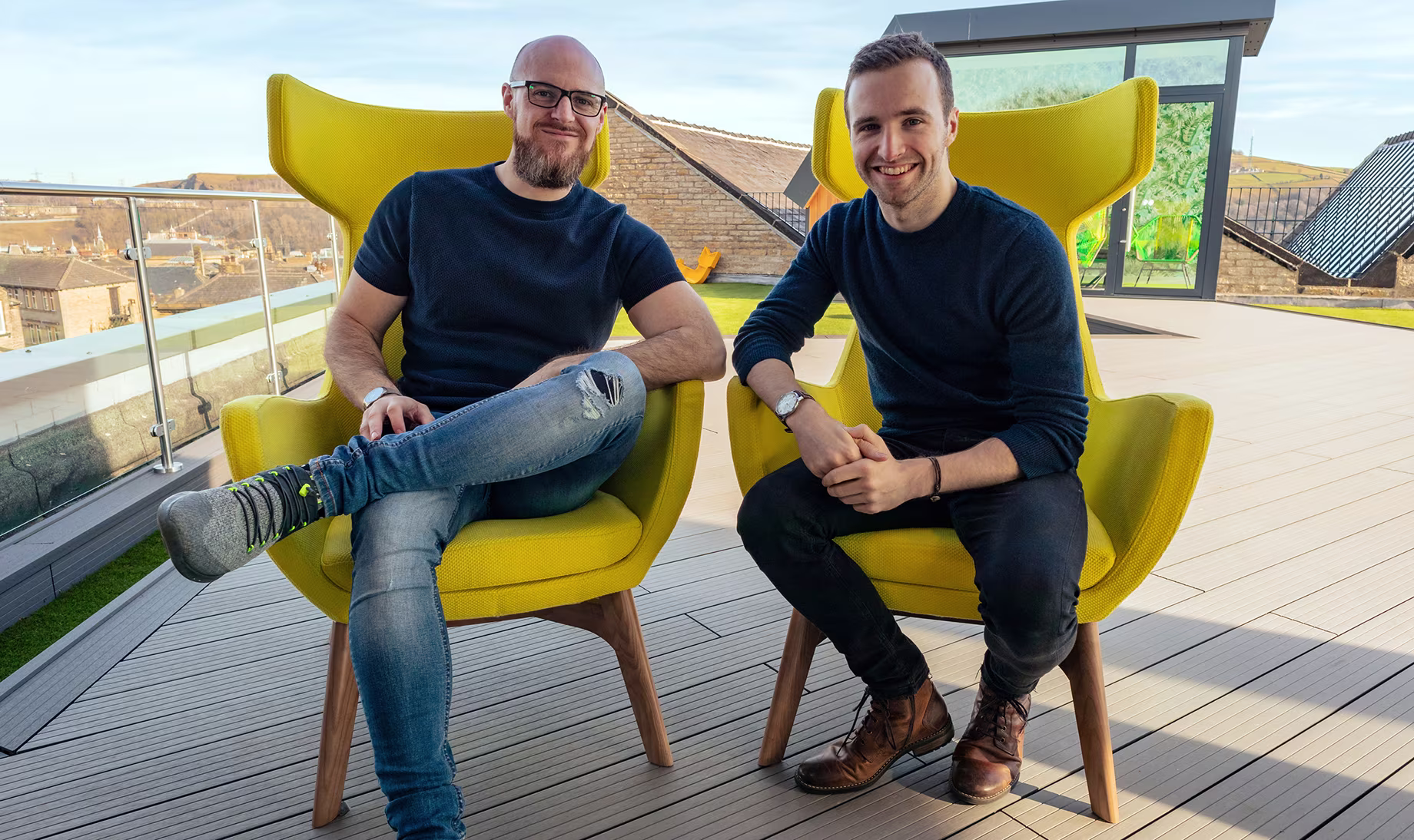 Chris and Martin relaxing on yellow chairs on the rooftop terrace, smiling for the camera.