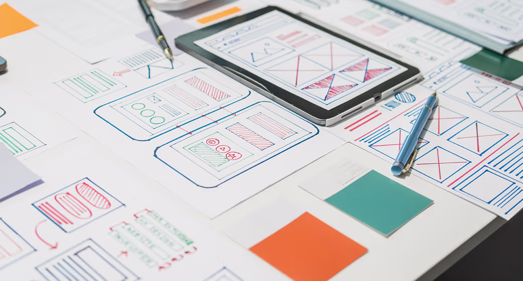 A tablet and papers with wireframes and design layouts on a desk, illustrating the user-centred design process.