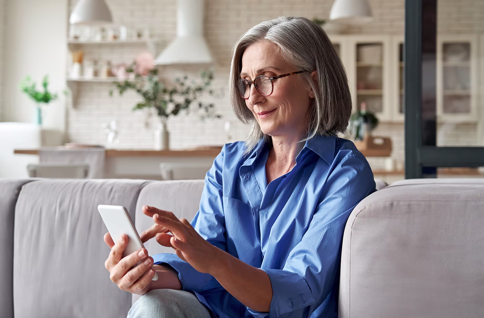 Smiling older woman using smartphone while sitting comfortably on a couch at home