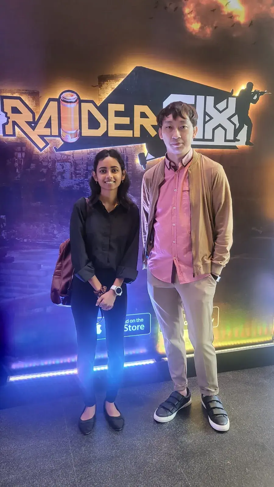 两位旅客在霓虹灯游戏馆招牌前合影