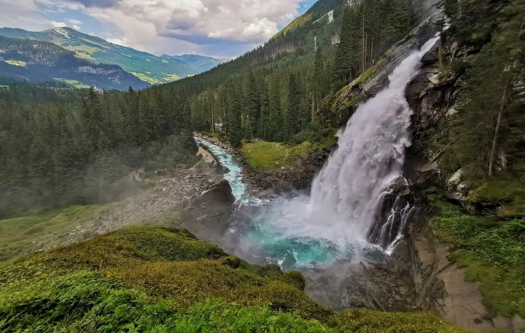 Waterfall on a mountain forming a river that flows into the forest, Krimml Waterfalls