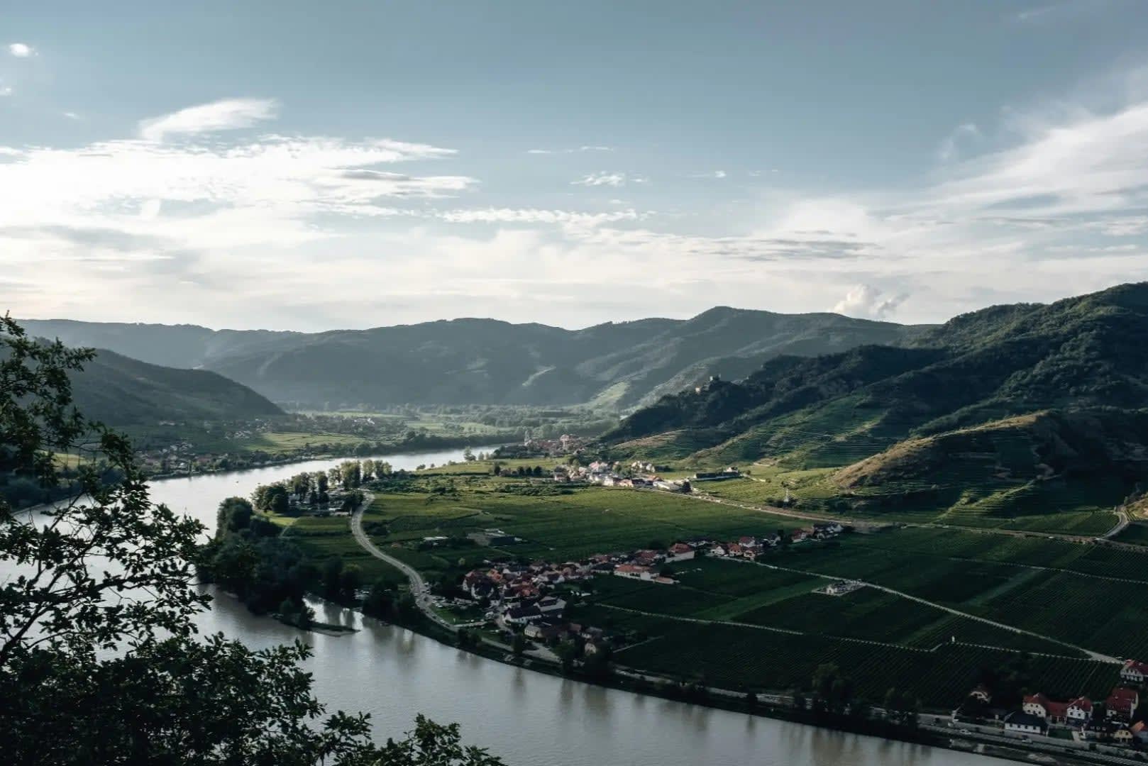 Cultivated fields in front of a river between mountains and a village, Wachau Valley
