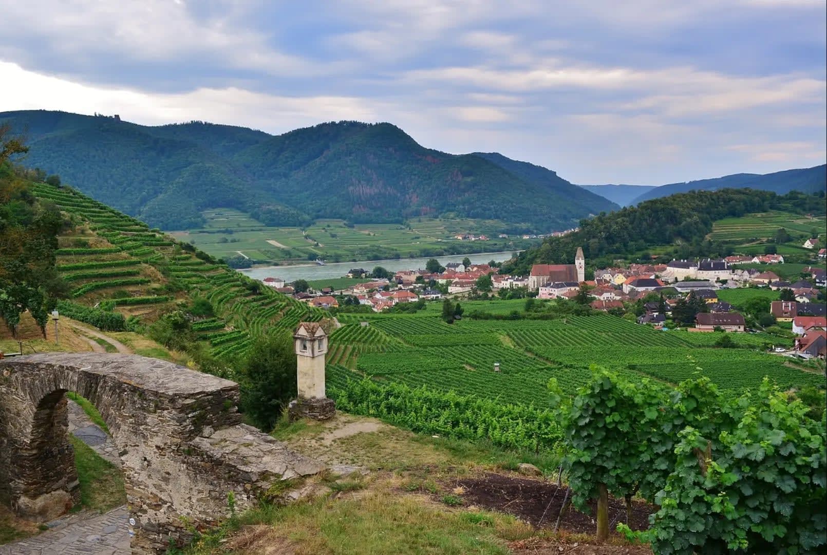 Cultivated fields in front of a river between mountains and a village, Wachau Valley