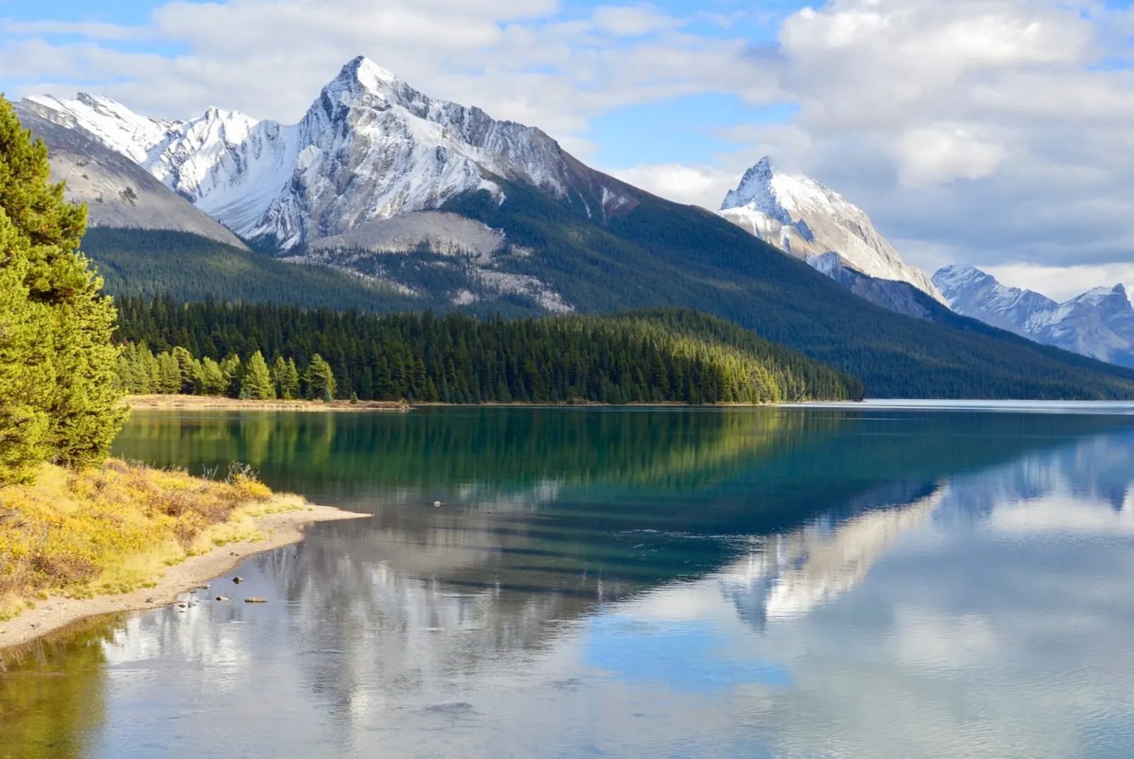 Jasper National Park in Canada showcasing a blue lake surrounded by wooded mountains with snow-capped peaks.