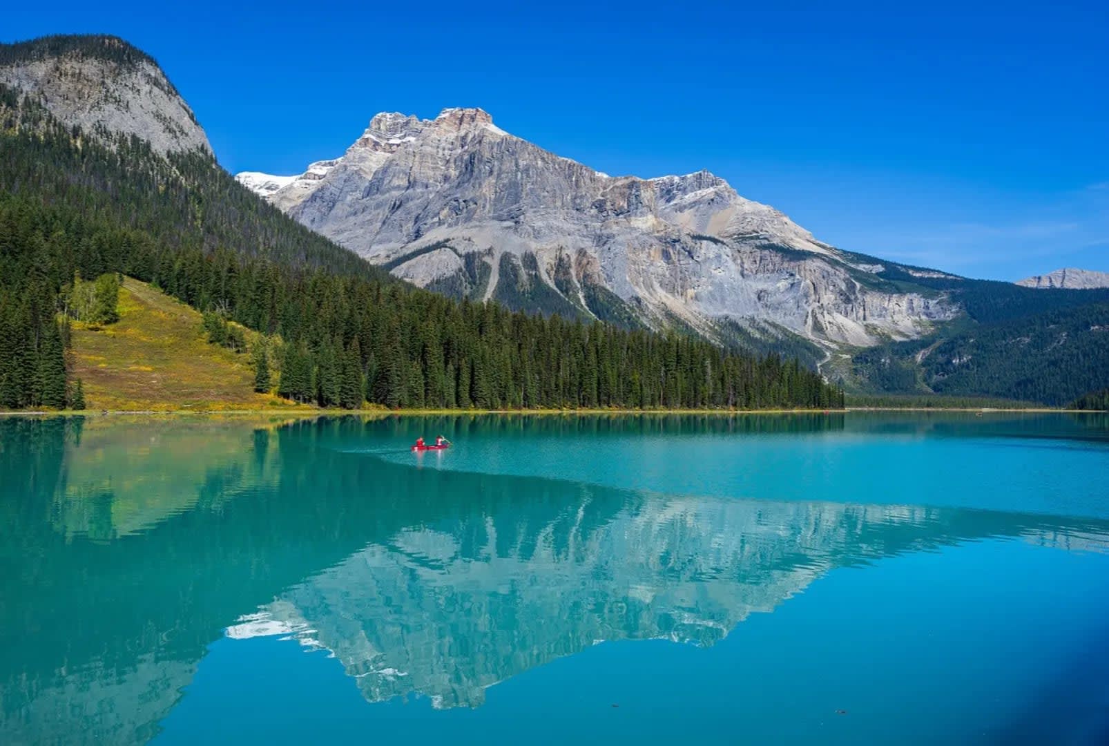 Yoho National Park in Canada featuring a blue lake surrounded by wooded mountains, with a raft and a person on the water.