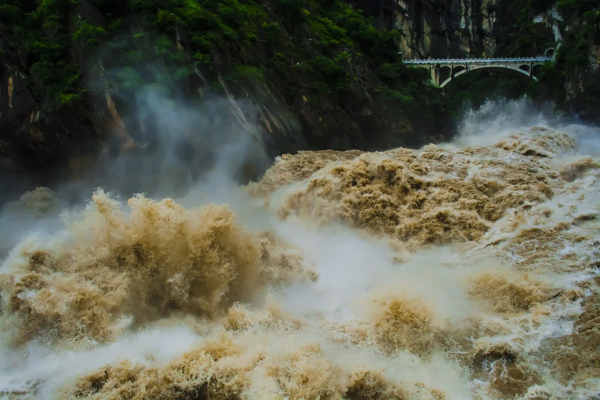 Raging river between mountains with vegetation and a bridge in the distance, Hutiao-Xia