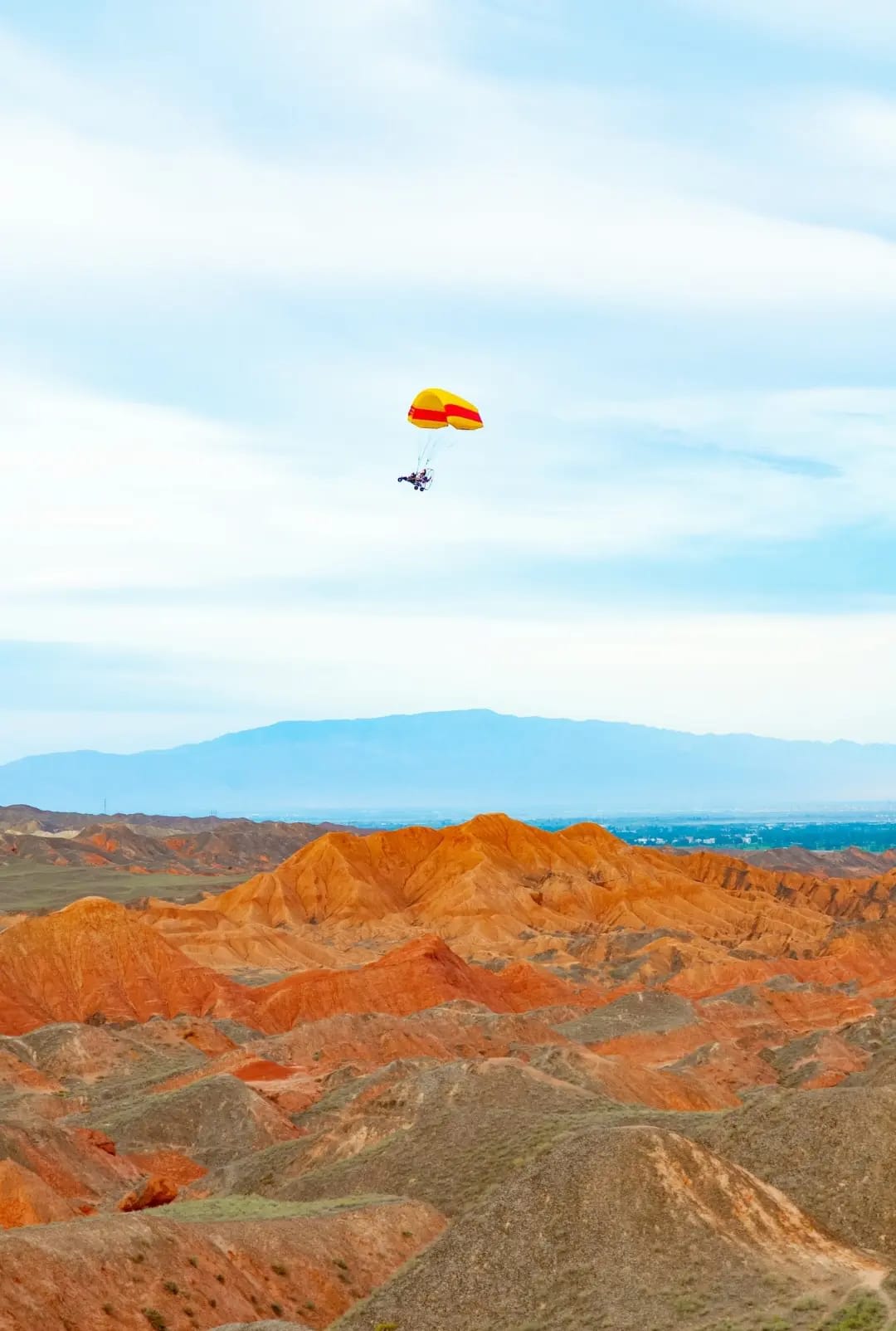 Soil hills in red, orange, brown, and white colors,Small plane with a parachute , Zhangye Danxia Landform