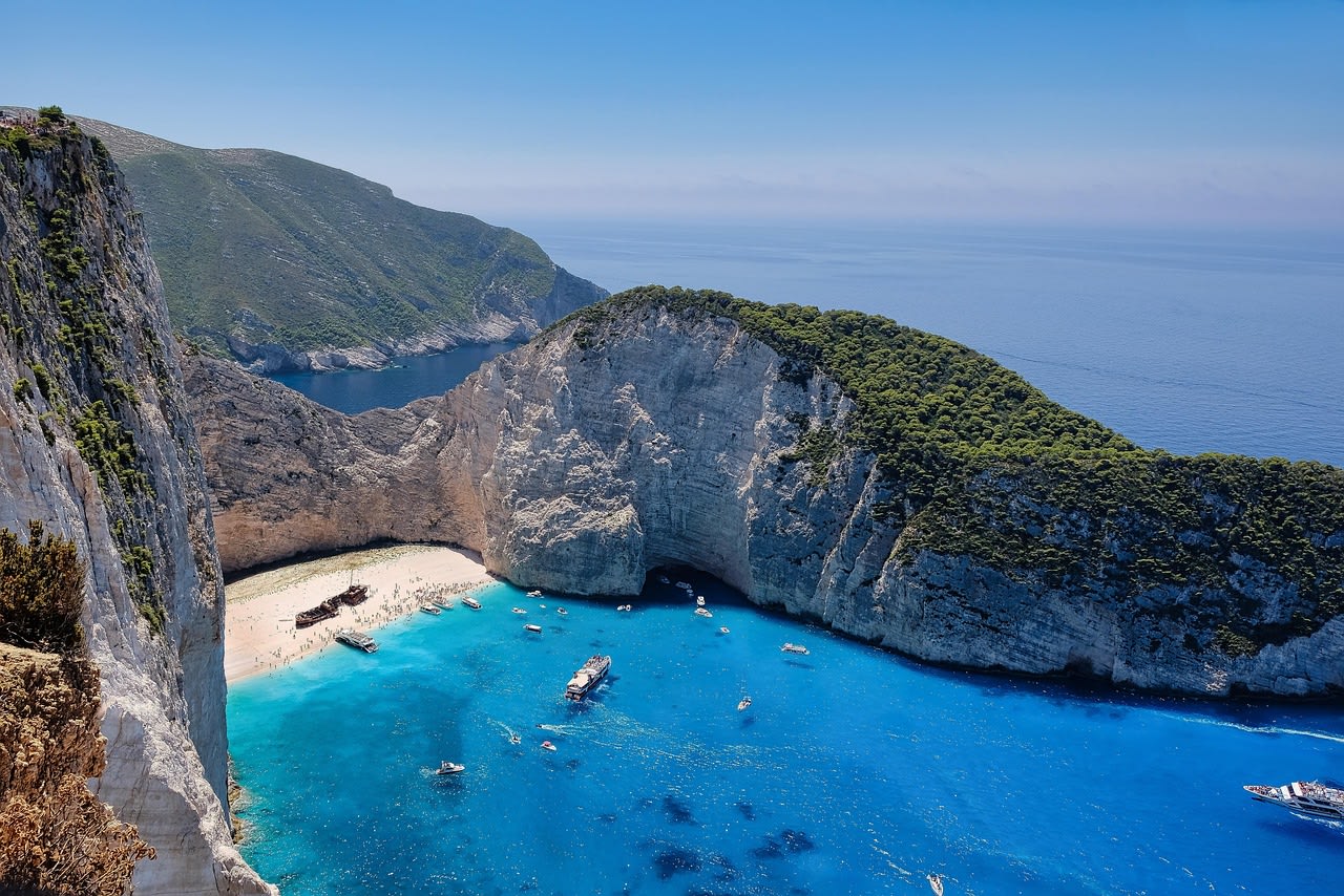 White limestone cliffs of Navagio beach reflected in the transparent turquoise Ionian Sea at the cove entrance