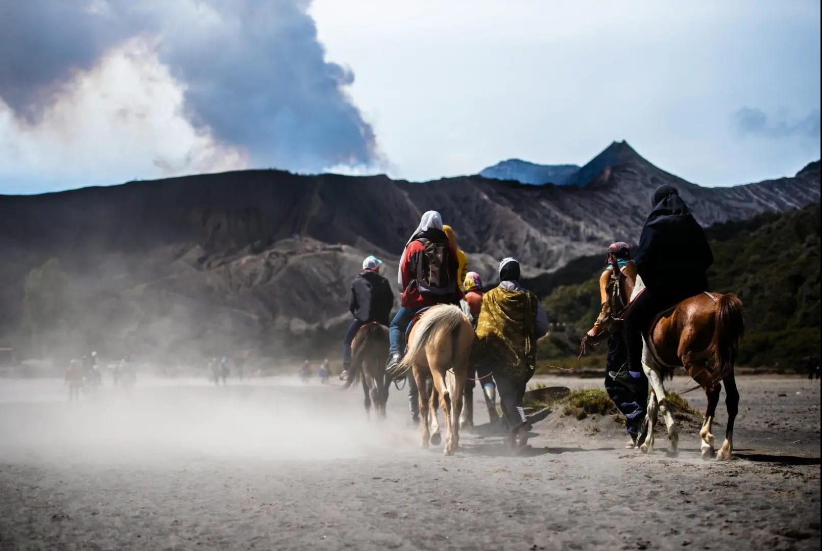 People on horseback heading towards mountains with smoke, Gunung Bromo