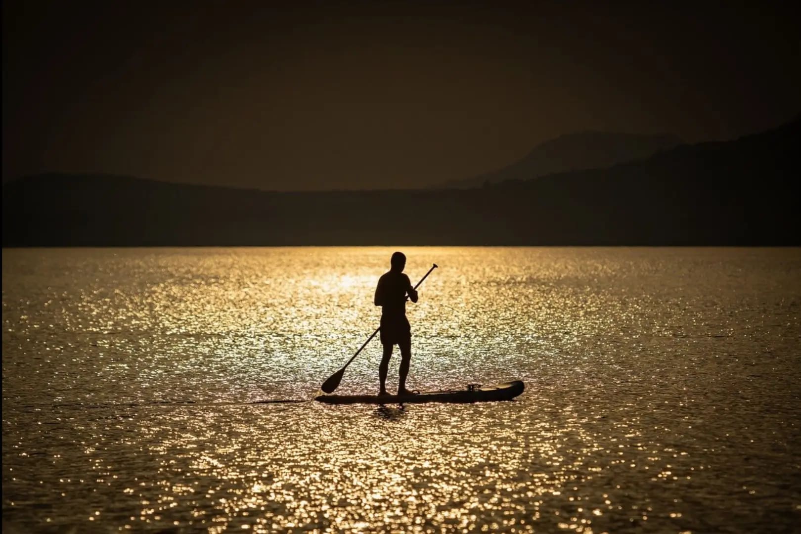 man standing on a paddleboard and rowing on a lake at sunset, Lake Biwa