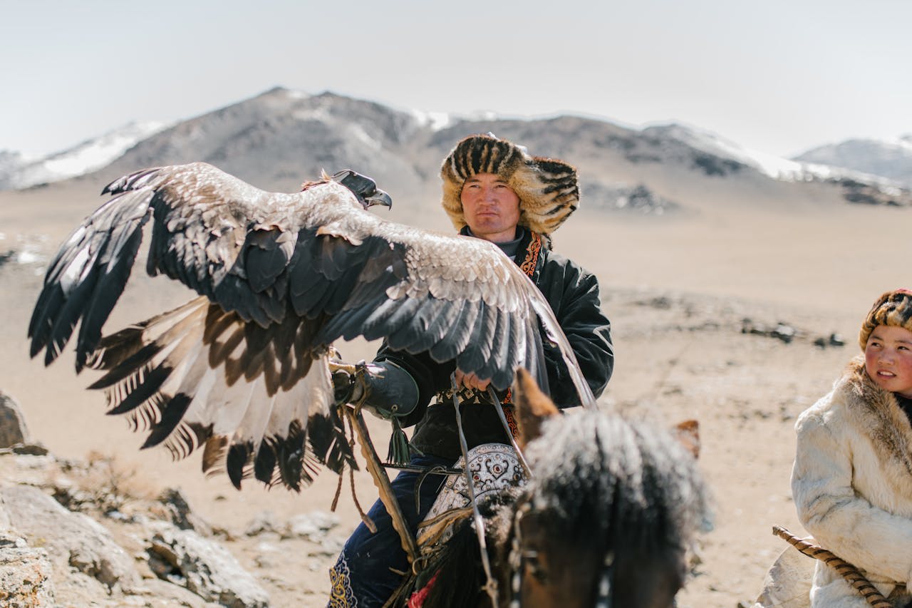 Kazakh eagle hunter on horseback with golden eagle against the snow-capped Mongolian Altai mountains
