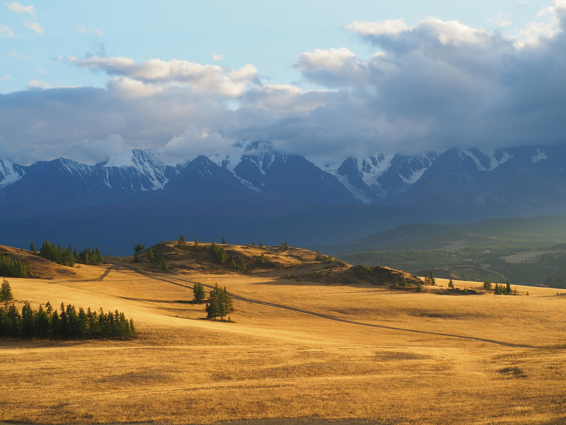 Nomadic Kazakh ger camp in a valley of the Mongolian Altai with horses and glacial peaks behind