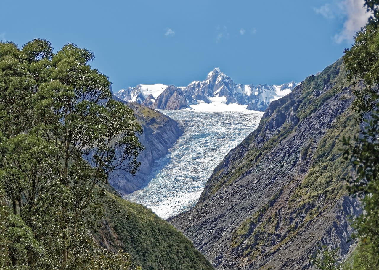 Hikers on Fox Glacier ice with crampons against the backdrop of the Southern Alps peaks