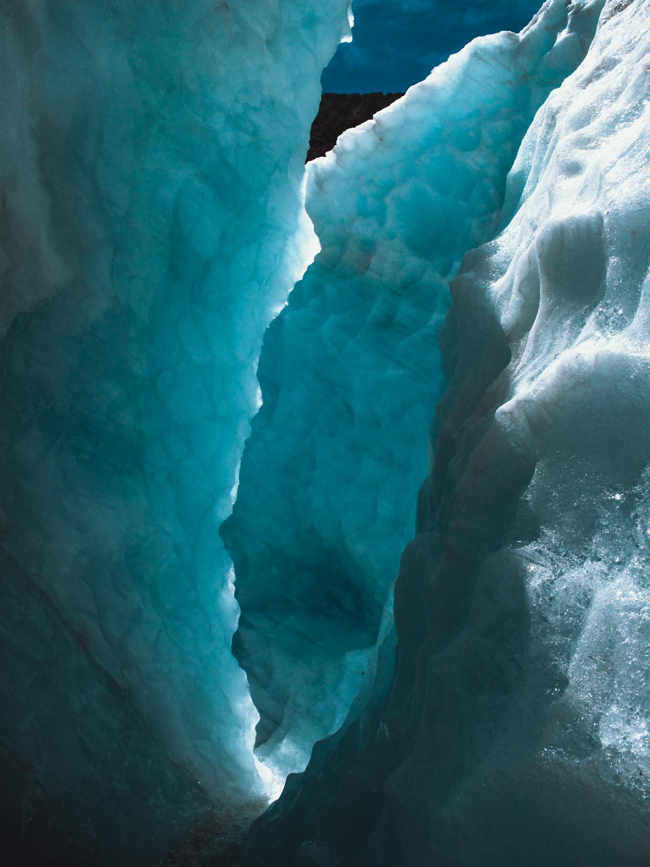 Blue ice crevasses on the surface of Franz Josef Glacier with mountain peaks behind in New Zealand