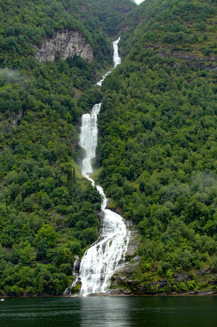 Cruise ship sailing through the narrow waters of Geirangerfjord surrounded by Norwegian mountains