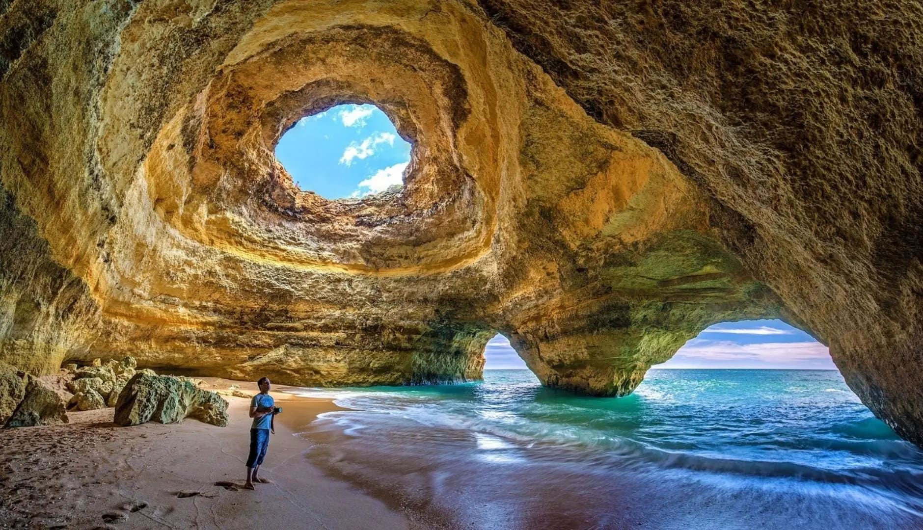 A large cave within a mountain by the beach in the Algarve, with a hole in the ceiling.