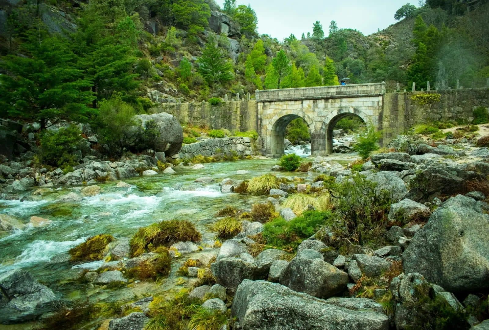 river flowing through rocks with a bridge in the background, Peneda-Gerês