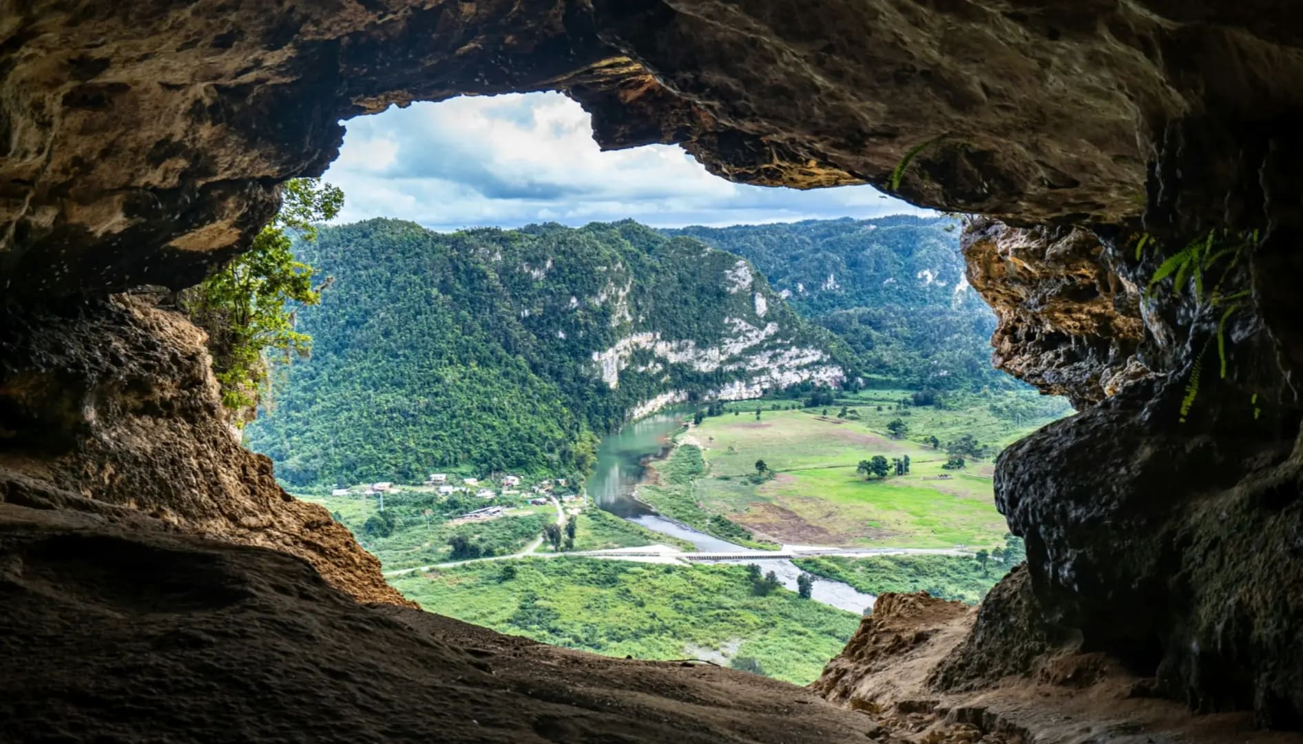 View from inside Cueva Ventana showcasing a winding river surrounded by lush vegetation and a mountain adorned with trees, creating a serene natural landscape.