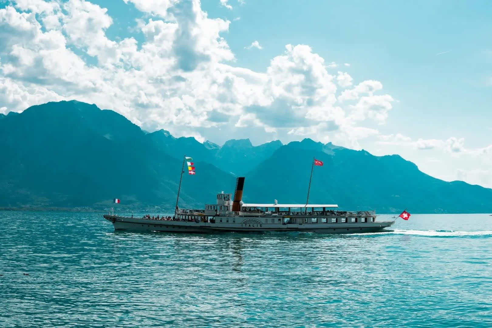 long boat on a lake with mountains in the background, Lac-Leman