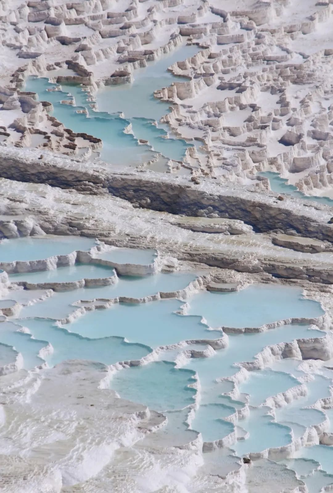 Terraces of Pamukkale with mineral-rich turquoise water cascading down white, natural limestone formations.
