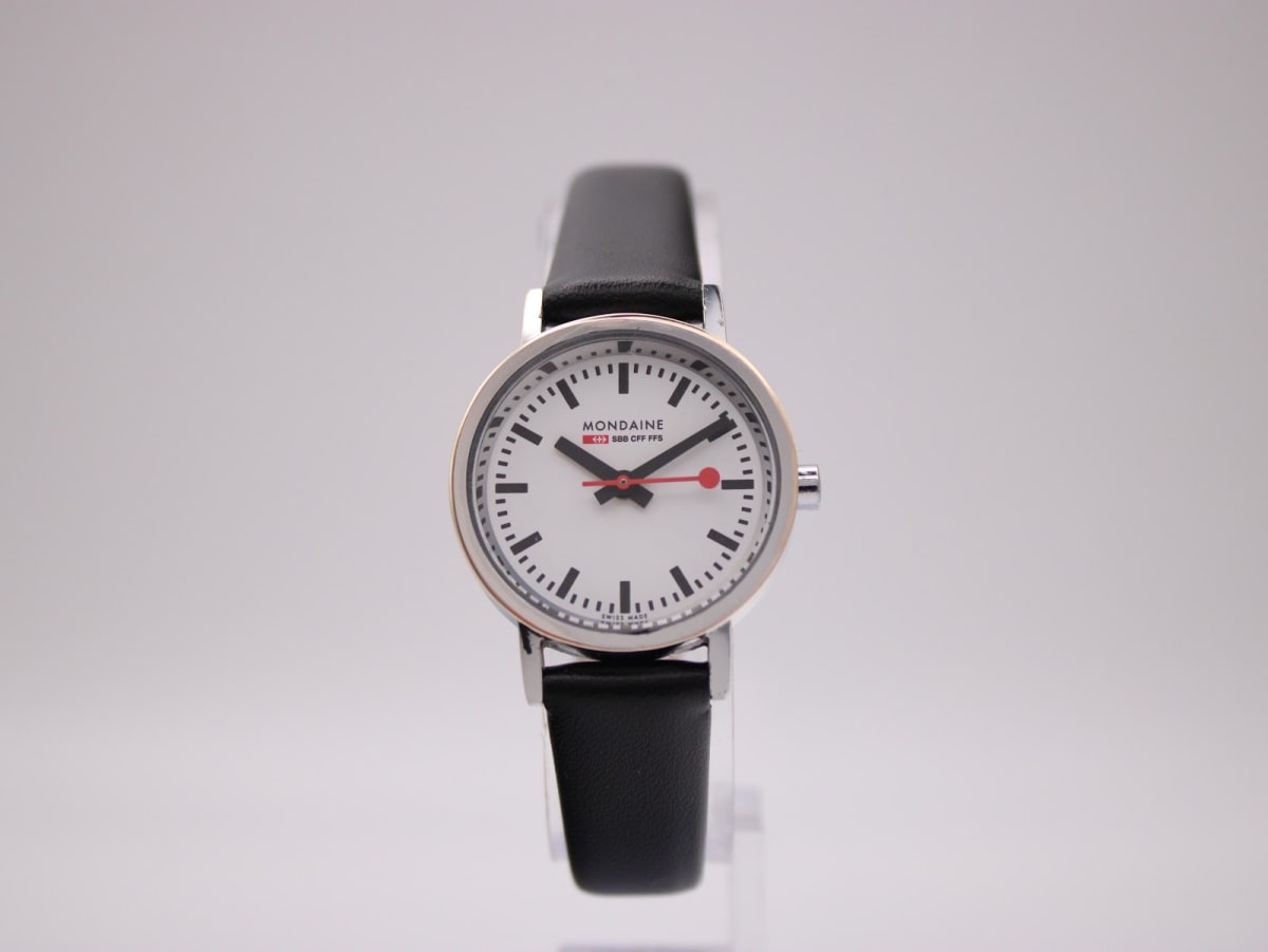 Front view of the Mondaine 3831 watch with white dial, silver case, and black leather strap on a stand.